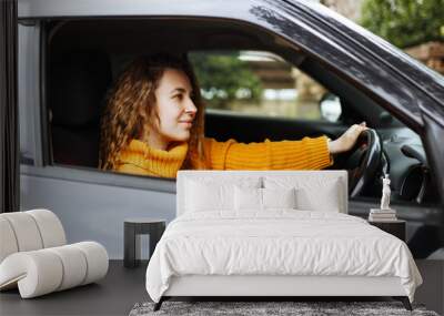 Portrait of young beautiful woman in yellow sweater sitting in the car. Wall mural