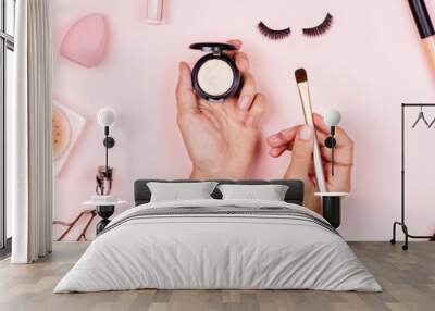 Flat lay of professional Cosmetics set on pastel pink background. Woman holding hands makeup brush Wall mural