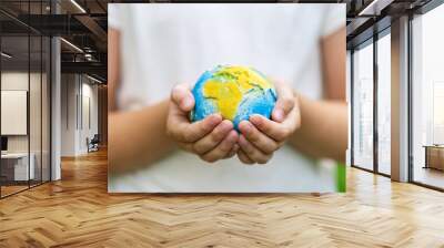 Kid holding small planet in hands against spring or summer green background. Ecology, environment and Earth day concept.  Wall mural