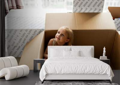 Lifestyle portrait of happy little caucasian girl six years old with blonde hair playing at home with cardboard boxes in new house at moving day. Wall mural