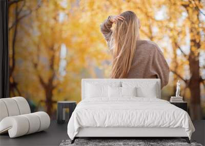 Portrait of a beautiful young woman with long blonde hair enjoying autumn in the park from behind. Background of ginkgo trees with yellow foliage. Fall season. Wall mural