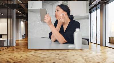 Beautiful brunette woman removing makeup from her face with mirror. Cute beautiful natural beauty girl cleaning face with cotton sponge. Cosmetology and spa, problem skin care, acne treatment concept Wall mural