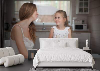 Happy family mother and child posing at home. Beautiful young mom and little daughter having fun and preparing vegetables for salad in a white kitchen in a Scandinavian style interior. Healthy food. Wall mural