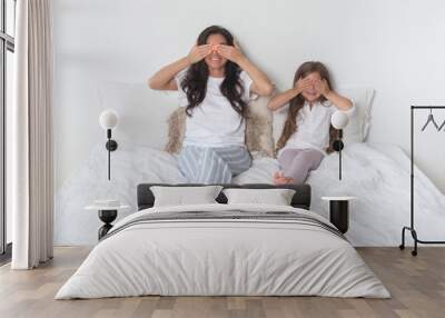 Happy loving family lying relaxing and enjoying in bedroom together. Mother and her cute preschool daughter child girl in pajamas playing and hugging in white bed in the morning. Happy mother's day. Wall mural