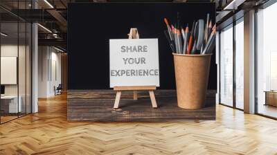 A white sign that says share your experience is on a wooden stand Wall mural