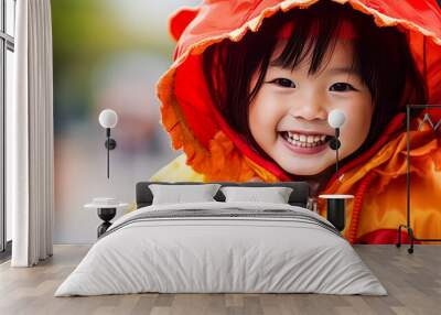 A young girl in a yellow jacket is smiling and posing for a picture. The scene takes place in front of a tree with orange pumpkins hanging from it. The girl's outfit and the pumpkins create a festive Wall mural