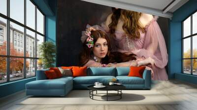 Two red haired young women in pink fairy dresses and pink flowers in hair holding roses. Fairytale romantic portraits of girls. Wall mural