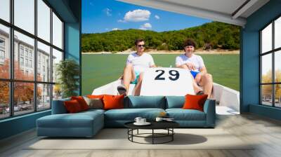 Two young men on water pedal boat tourist catamaran on mountain lake on sunny day. Summer leisure activities in public park. European caucasian white young male men. Lifestyle portrait Wall mural