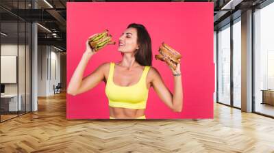 Beautiful fit woman in yellow bright fitting sportswear on pink background happy hold healthy avocado and roast beef sandwich Wall mural