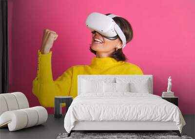 Beautiful woman in bright yellow sweater on pink background in virtual reality glasses happy jumping clenching fist winner gesture Wall mural