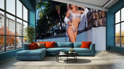 Fit caucasian pretty sexy woman in bikini and sunglasses on vacation on tropical beach at sunset natural light.    Wall mural