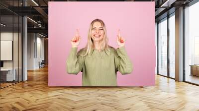 Pretty european woman in casual knitted sweater on pink background happy amazed excited point up with index finger copy space Wall mural