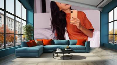 Stylish fashion young caucasian woman blogger at home take sephoto selfie on mobile phone in mirror in bedroom, wearing brick color shirt and white skirt. Trendy combination clothing for social media. Wall mural