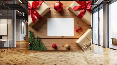 A flat lay of a blank sheet of paper in the center, surrounded by wrapped holiday gifts, red Christmas ornaments, and pine branches on a wooden table. A simple yet festive holiday scene  Wall mural