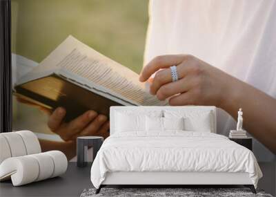 Christian woman holds bible in her hands. Reading the Holy Bible in a field during beautiful sunset. Concept for faith, spirituality and religion Wall mural