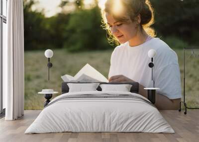 Christian woman holds bible in her hands. Reading the Holy Bible in a field during beautiful sunset. Concept for faith, spirituality and religion Wall mural