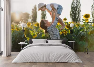 Mother with little baby son in sunflowers field during golden hour. Mom and son are active in nature Wall mural