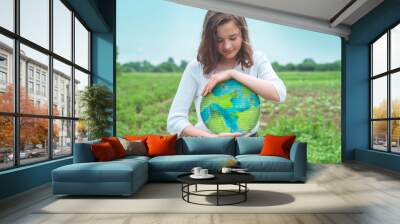 Teen girl holding planet in hands against green spring background. Earth day holiday concept. Protection and love of earth Wall mural