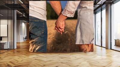 Unrecognizable man and woman holding hands in the middle of a wheat field. Farmers standing in a wheat field Wall mural