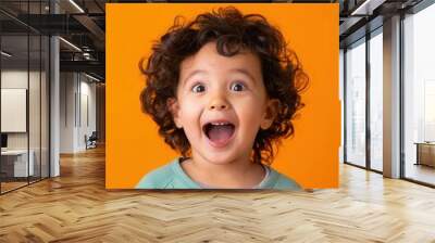 A cheerful young child with curly hair beams with delight, showcasing pure joy in front of a bright orange background. Generative AI Wall mural