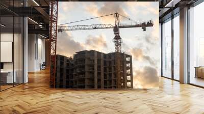 Cranes are lifting materials at a busy construction site as the sun sets, casting a warm glow over the ongoing building project Wall mural