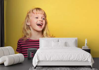 Close-up portrait of a cute attractive cheerful excited girl. Cute sweet smiling child in a pink striped t-shirt. Blonde girl 5 years old on a bright yellow background with a place for text Wall mural