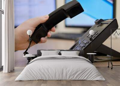 A man hand holds a phone near the monitors of office computers. Starting a telephone conversation at the workplace, close-up desk Wall mural