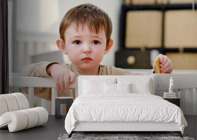 Child eats cookies in a crib. Feeding a baby in bed like in a playpen. Kid aged about two years (one year nine months) Wall mural