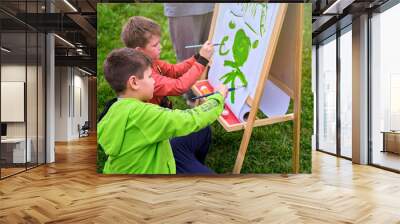 Mother teaches to paint with two boys pupils. Woman teacher artist paints with children on paper nature and trees by the river Wall mural