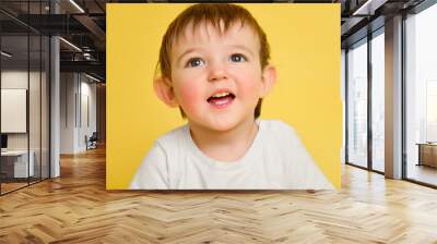 Portrait of a happy toddler baby on a studio yellow background. Smiling child in a white t-shirt. Kid aged one year and four months Wall mural