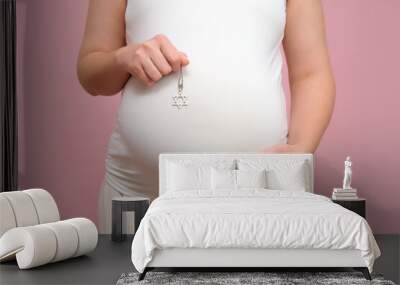 Pregnant woman holding religious Jewish symbol in hand, studio pink background Wall mural