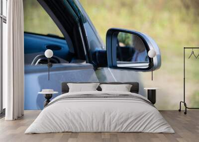 Close-up view of gray side mirror (or door mirror) of car in countryside in a sunny summer day. Blurred female driver reflects in mirror surface. Automobile industry theme. Wall mural