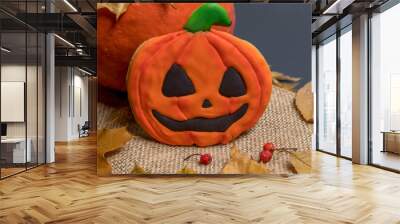 Jack O'Lantern gingerbread cookie lies on sackcloth (or burlap) leaning on real pumpkin by fallen birch leaves. Smiling pumpkin face. Halloween homemade baking theme. Wall mural