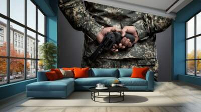 A man in an American camouflage uniform with a pistol in his hand behind his back. The readiness for hostilities and the turbulent political environment. Gray background. Wall mural