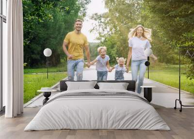 Happy family with two children joyfully run in the park on a sunny summer day. Parents, son and daughter in jeans and T-shirts. Love, tenderness and relationships in the family. Wall mural