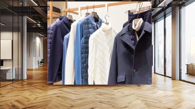 Stylish men's clothing collection on hangers and shelves in the store. Sweaters, jackets and trousers. Wall mural