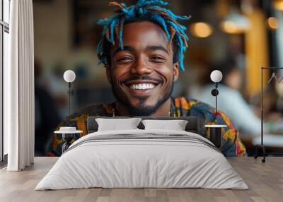 A man with blue hair and a smile is sitting at a table in a restaurant. He is wearing a colorful shirt and a necklace Wall mural