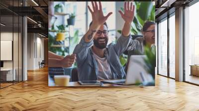 An important contract is signed in a busy corporate office by a man working on a laptop - he instantly jumps in celebration and gives his co-workers a high-five in recognition. Wall mural