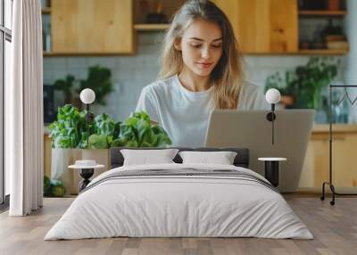 Close-up of woman in white shirt cooking salad at home. Healthy recipe book, menu. Girl using laptop to view video while making vegan salad. Wall mural