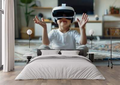 In his living room, a child wearing virtual reality glasses uses hand gestures to control Augmented Reality games. The little boy is sitting on a carpet. Wall mural