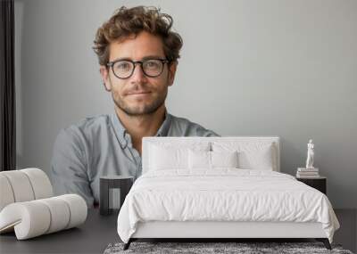 In this image, a man wears glasses and crosses his arms in front of a white background Wall mural