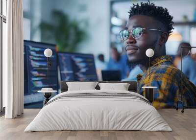 The image depicts a young african male programmer at the workplace, writing code on three monitors. Wall mural