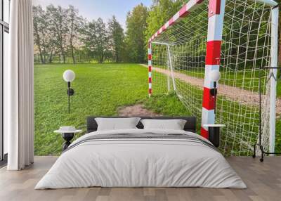 A soccer goal with a red and white striped pole. The grass is green and the sky is blue Wall mural