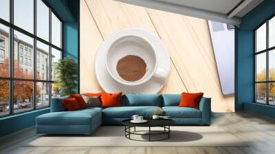 A white coffee cup with a small amount of coffee powder on top of it. The cup is placed on a wooden table next to a laptop. Concept of relaxation and leisure Wall mural