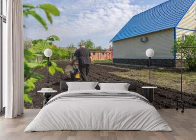 Cottage, plot of land in front of the house. Man ploughing land with cultivator on sunny spring day. Concept of gardening, gardening, dacha Wall mural