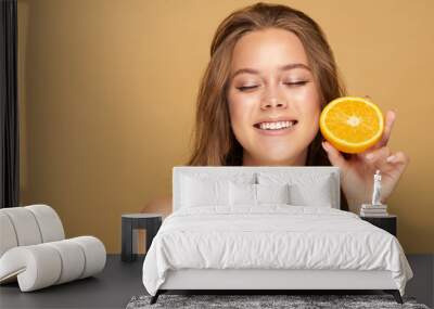 Young beautiful woman holding slices of orange in front of her eyes Wall mural