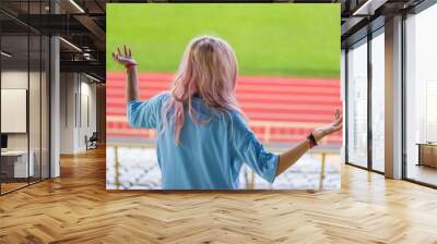 girl football fan in light blue t-shirt support her favorite team and looking soccer game on stadium tribune from above, copy space Wall mural