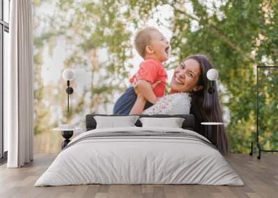  A happy young mother plays and has fun with her little son in the sun on a warm spring or summer day. The concept of a happy family, motherhood. Mother and child walk Wall mural