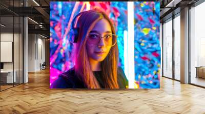 a young, attractive woman wearing headphones listens to music in the neon night light. girl DJ. Creative portrait in neon lighting. The concept of youth culture. Wall mural