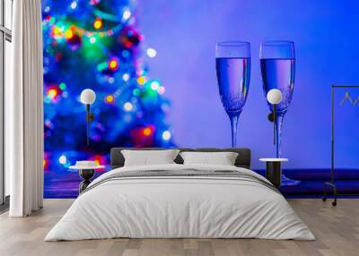 Glasses of champagne in a festive atmosphere, close-up. Christmas lights and two glasses on the background of a fir tree Wall mural